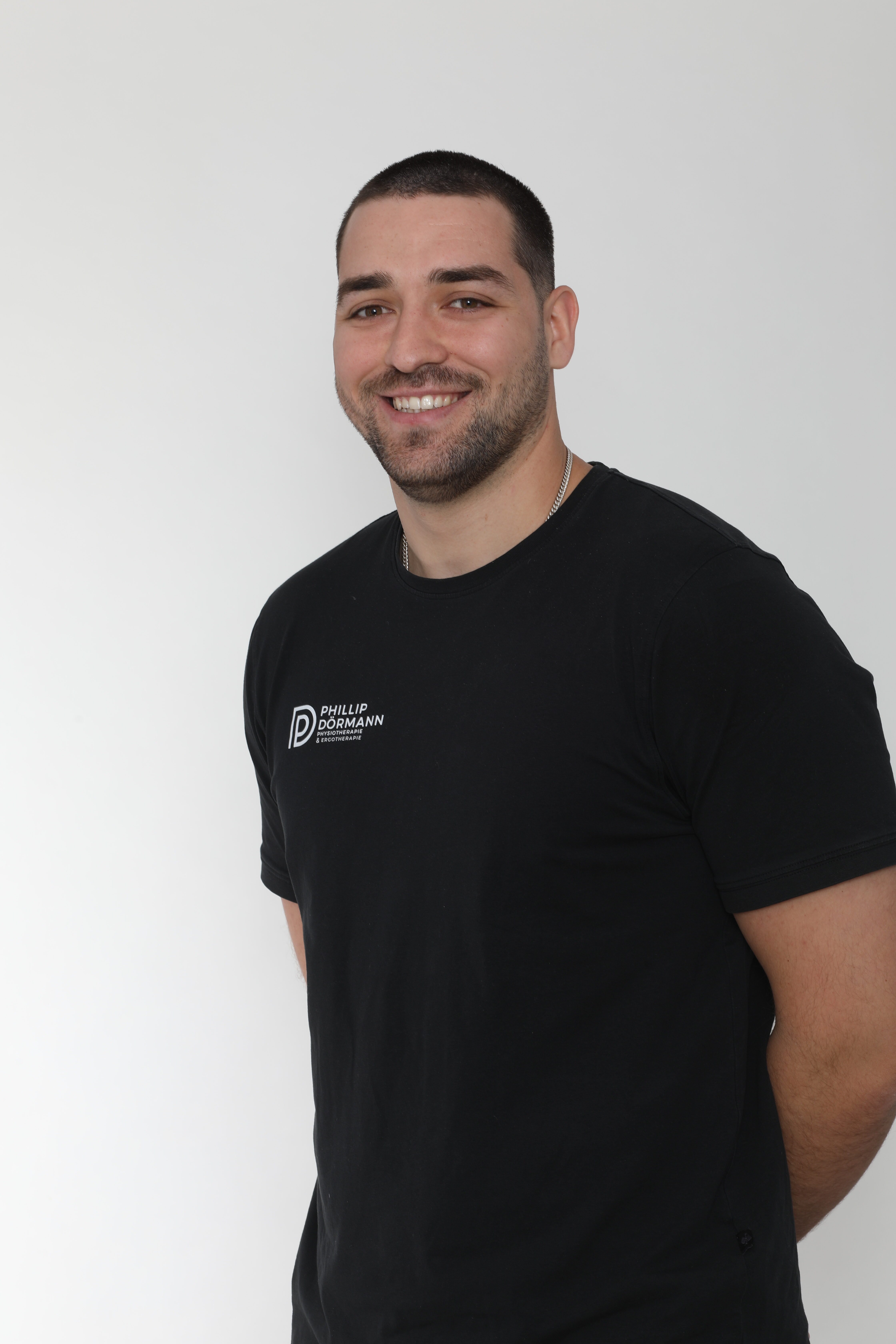 Mann mit kurzem Haar lächelt in schwarzem T-Shirt vor weißem Hintergrund.