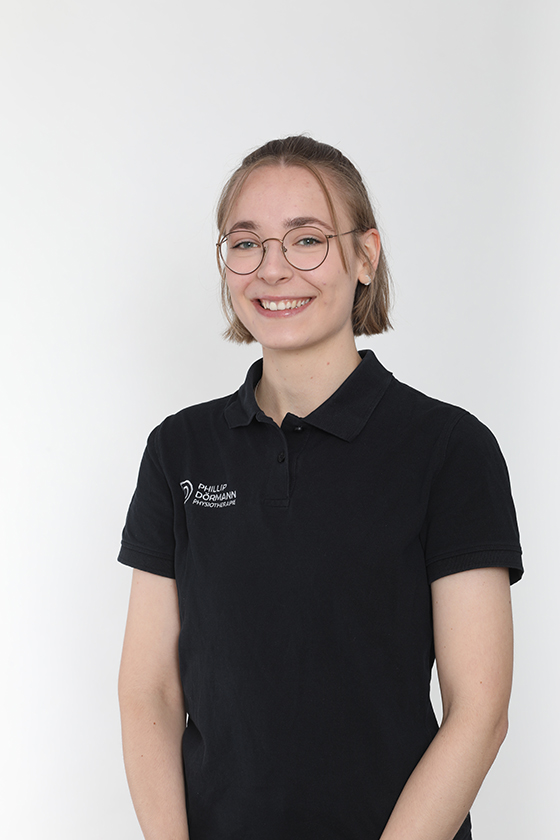 Junge Person mit Brille und zufriedener Mimik, trägt schwarzes Polohemd, heller Hintergrund.