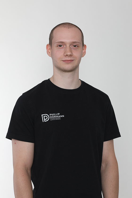 Junger Mann mit neutralem Gesichtsausdruck, schwarzes T-Shirt mit Logo und weißem Hintergrund.
