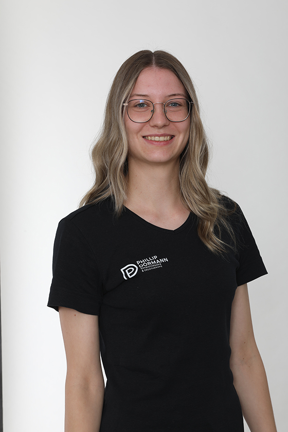 Eine lächelnde Person mit Brille und schwarzem T-Shirt vor hellem Hintergrund.