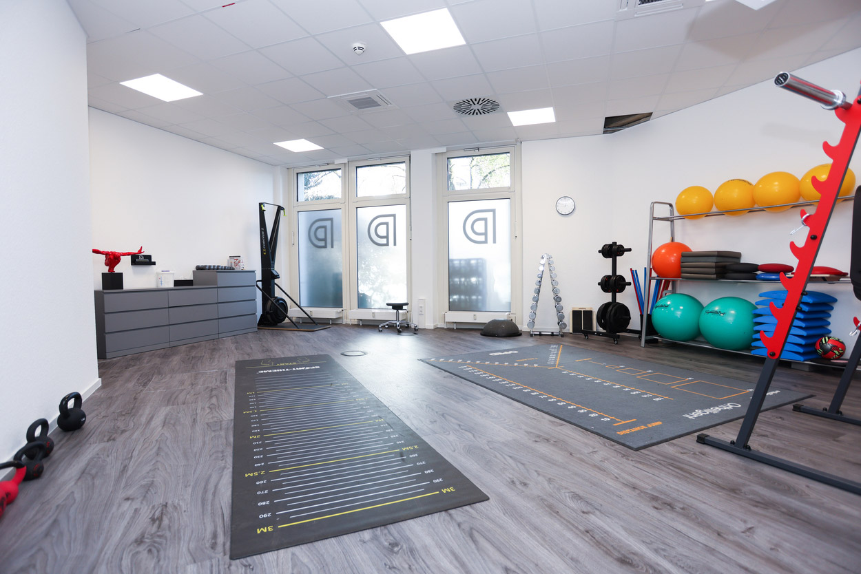 Fitnessstudio mit Holzboden, bunten Gymnastikbällen, Trainingsgeräten und großen Fenstern.