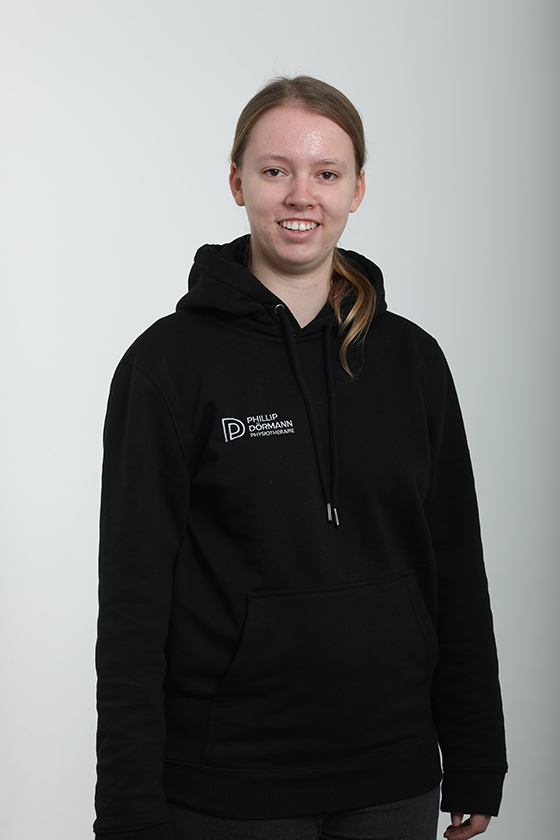 Eine lächelnde Frau in einem schwarzen Kapuzenpullover vor einem weißen Hintergrund.