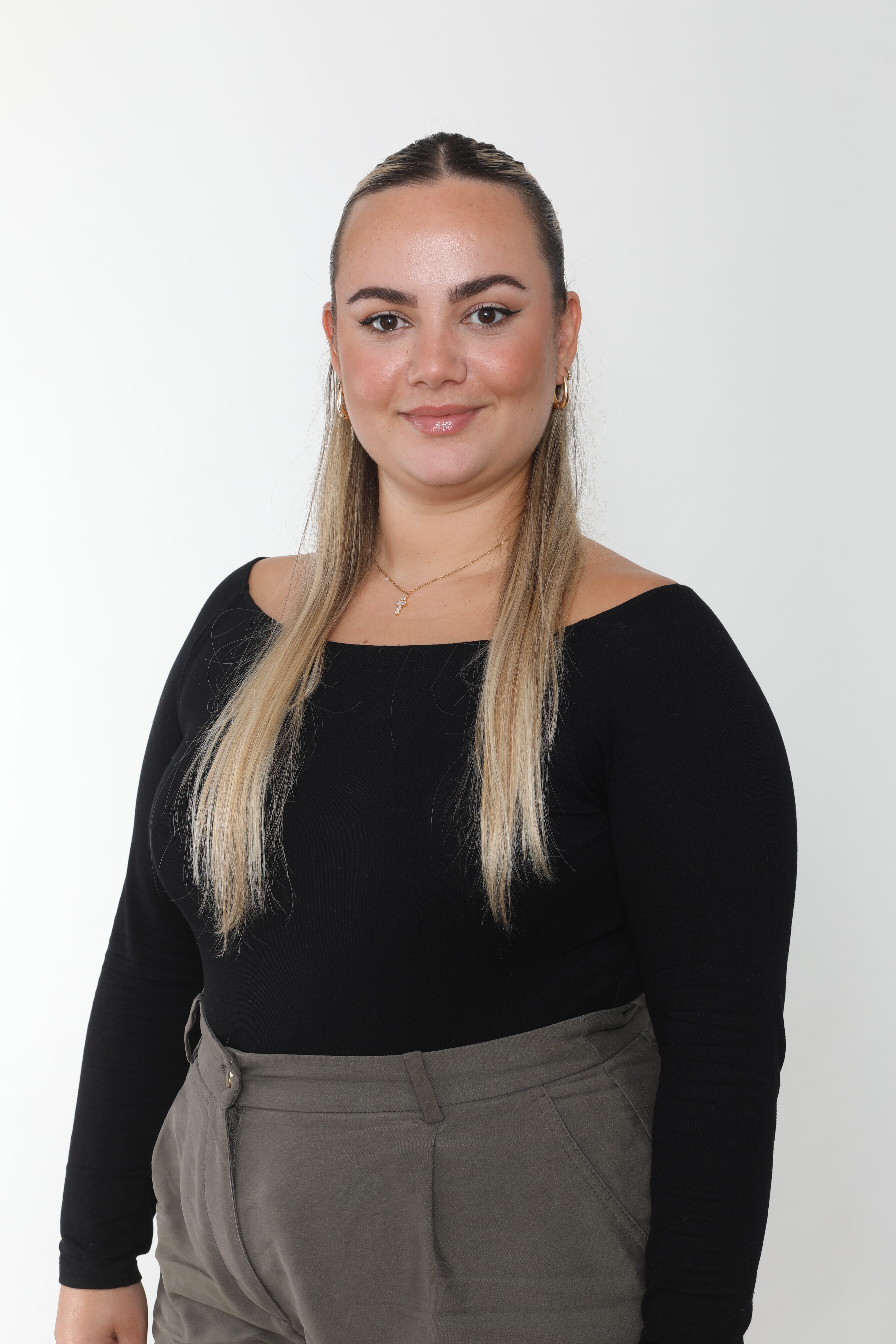 Person lächelt, trägt schwarzes Oberteil, lange blonde Haare, grüner Rock. Neutrale Hintergrunde.