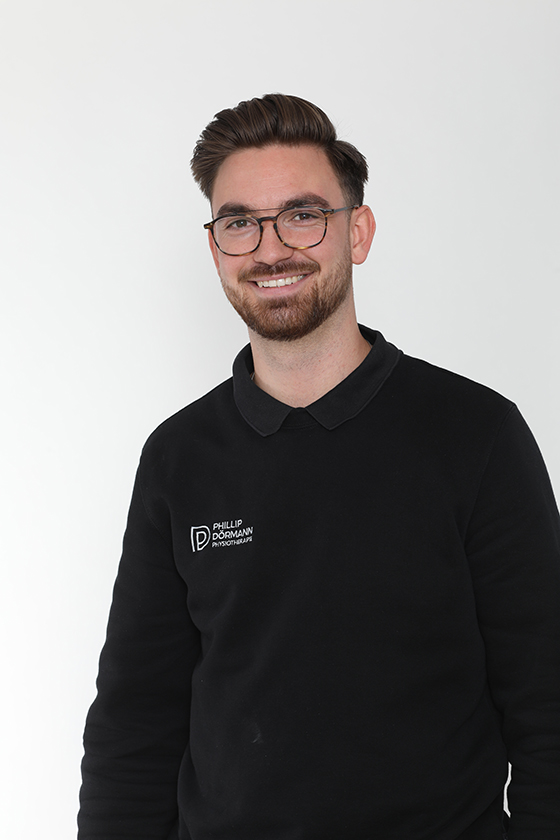Ein Mann mit Brille lächelt in schwarzem Pullover vor weißem Hintergrund.