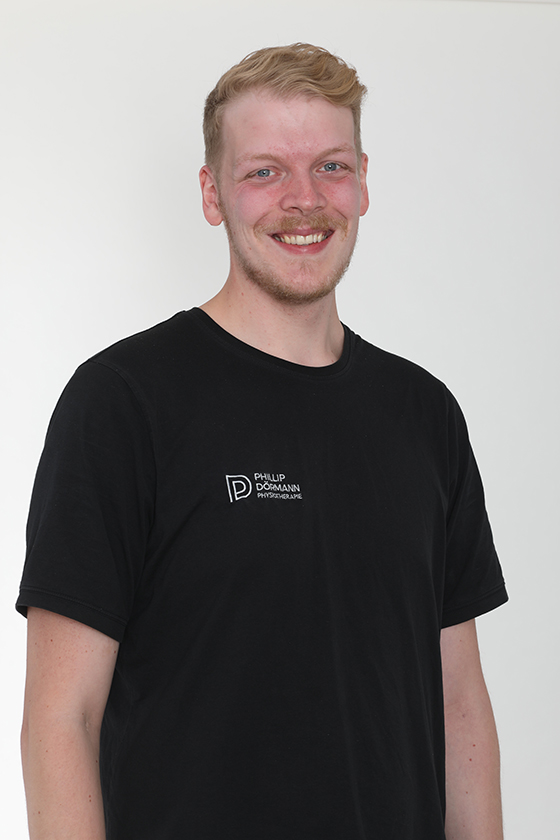 Ein lächelnder Mann mit Bart in schwarzem T-Shirt vor weißem Hintergrund.