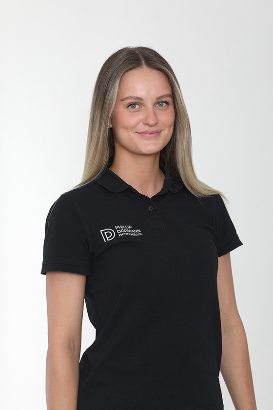 Frau mit lächelndem Ausdruck, trägt ein schwarzes Shirt mit Logo, lange blonde Haare.