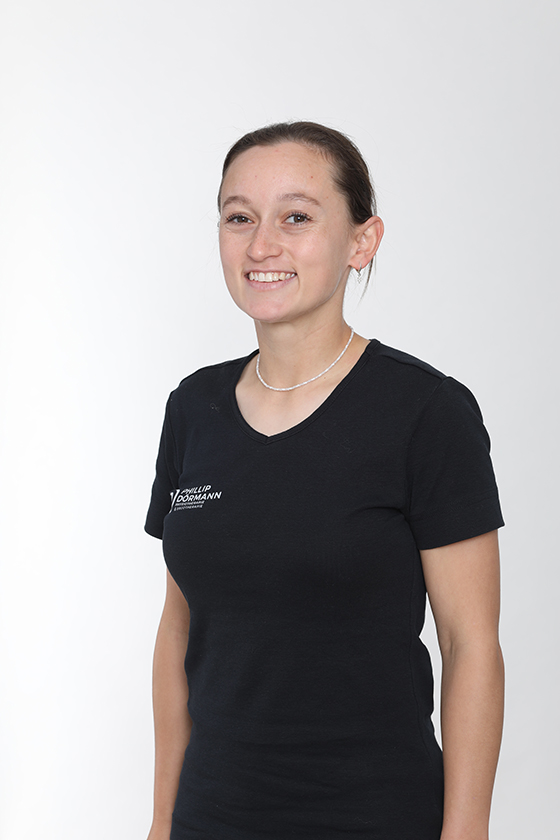 Junge Frau lächelt gelassen, trägt schwarzes T-Shirt, helle Halskette, neutraler Hintergrund.