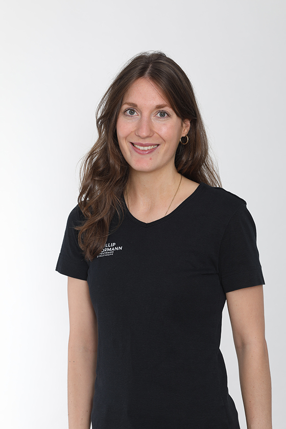 Eine Frau mit langem braunen Haar lächelt freundlich. Sie trägt ein schwarzes T-Shirt.
