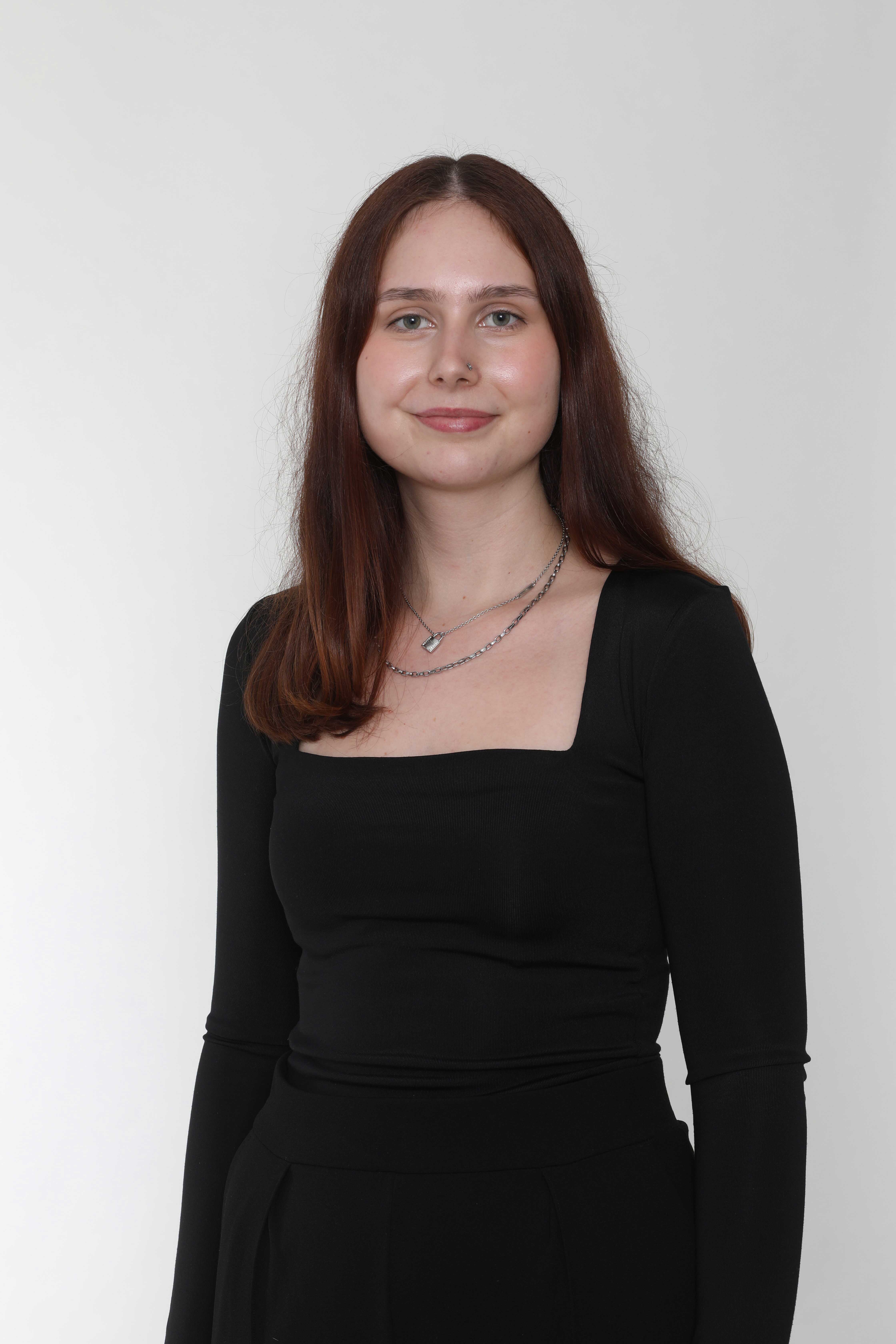 Eine junge Frau mit langen, braunen Haaren lächelt, trägt ein schwarzes Oberteil.