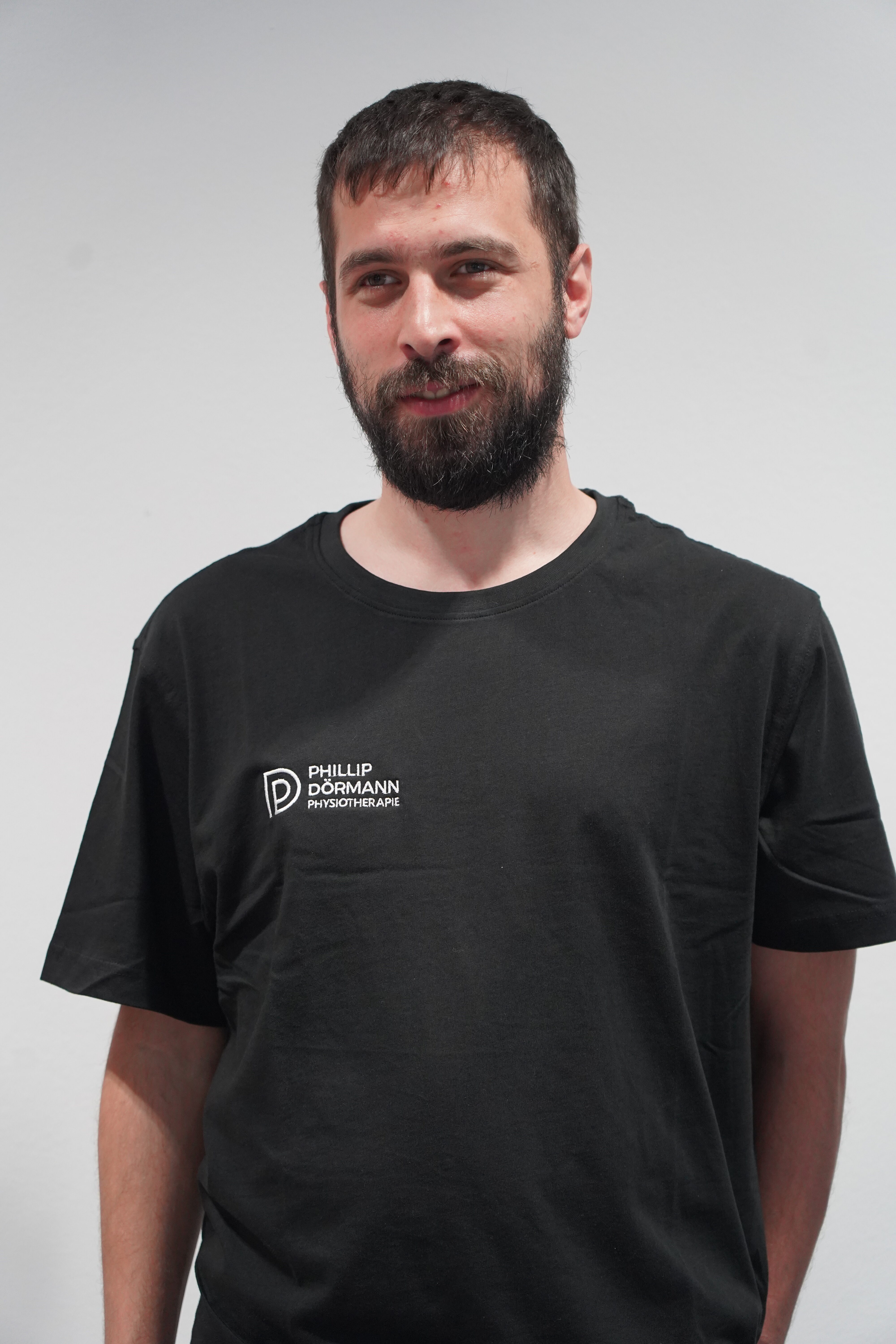 Laechelnder Mann mit Bart im schwarzen Shirt mit weissem Logo
