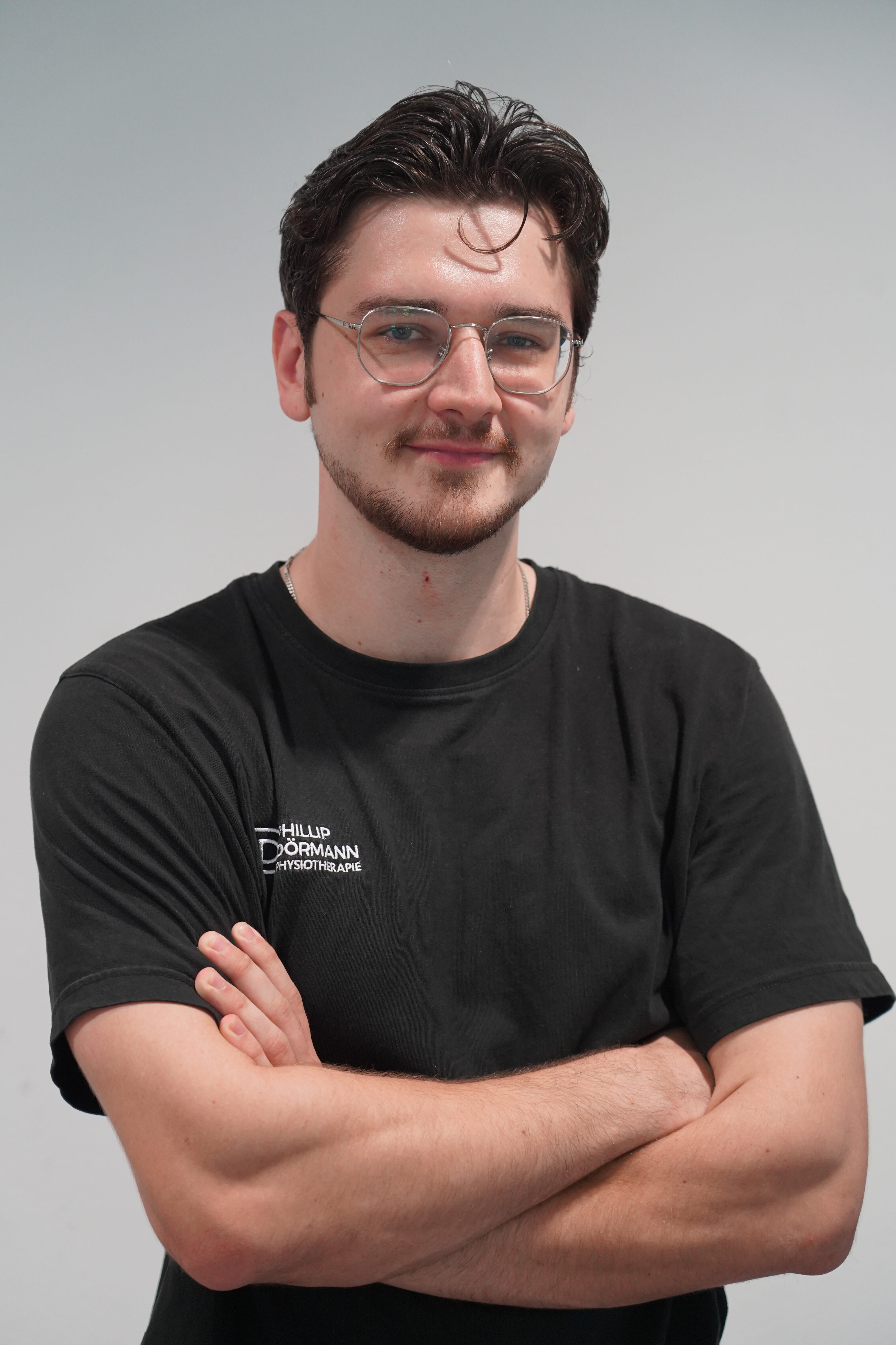 Mann mit Brille, freundlich, schwarzes Shirt, Arme verschraenkt, Locke