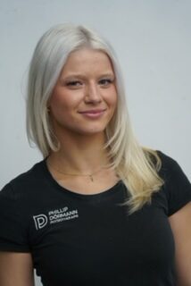 Laechelnde blonde Frau im schwarzen Shirt mit Logo vor hellem Hintergrund