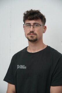 Junger Mann mit Brille und Bart traegt ein schwarzes T Shirt mit Logo